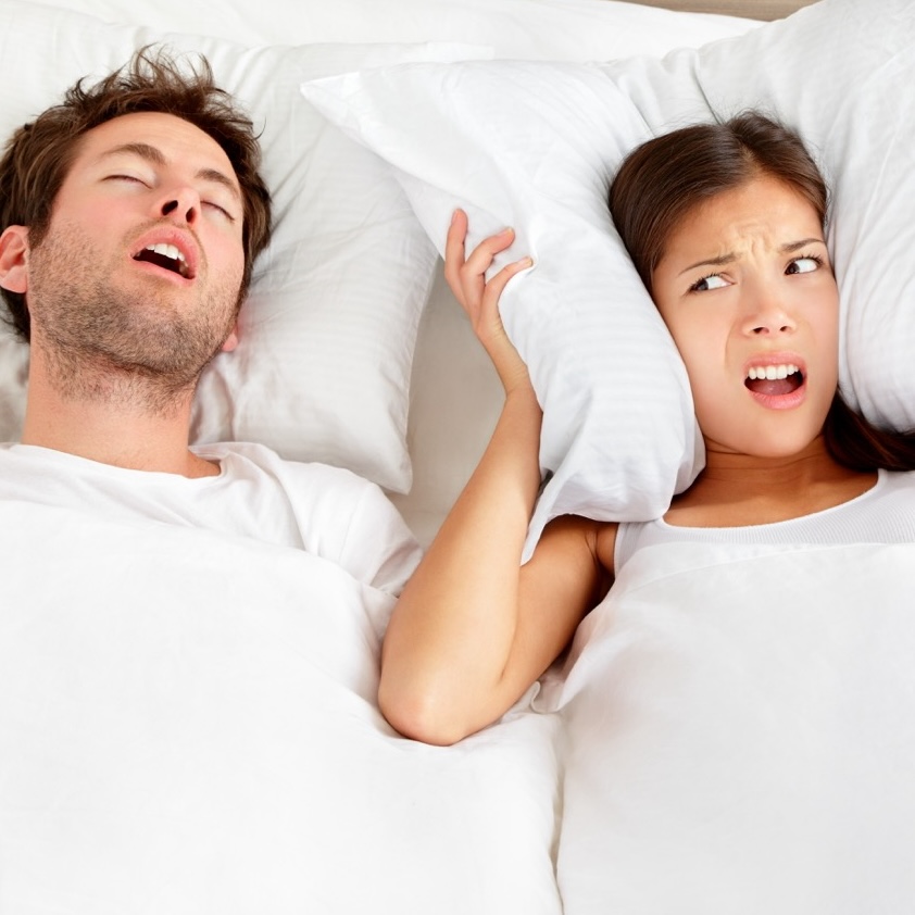 Snoring man. Couple in bed, man snoring and woman can not sleep, covering ears with pillow for snore noise. Young interracial couple, Asian woman, Caucasian man sleeping in bed at home.